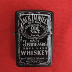 Черна метална запалка тип Zippo с дизайн на етикета Jack Daniel's Old No. 7 Tennessee Whiskey, позиционирана на червен фон.