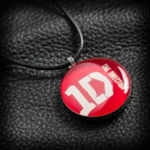 Кръгъл метален медальон на One Direction с бяло 1D лого върху червен фон под смола