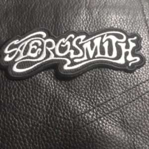 Бродирана нашивка Aerosmith Logo с бял надпис върху черно кожено яке.