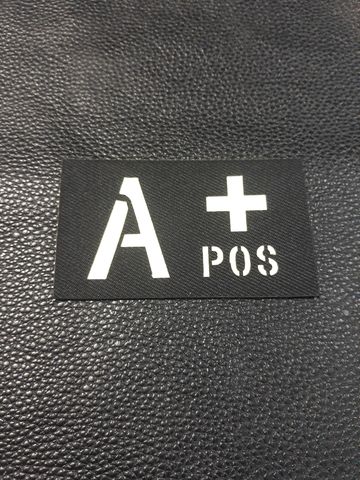 Светеща нашивка с кръвна група A+ POS в бяло върху черен фон.