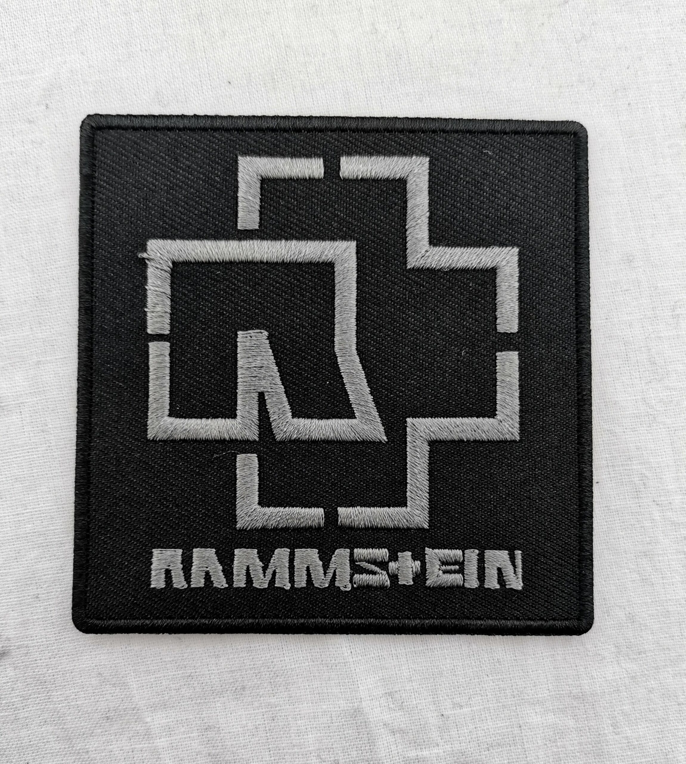 Квадратна нашивка RAMMSTEIN сиво лого с бродирани детайли върху черен фон.