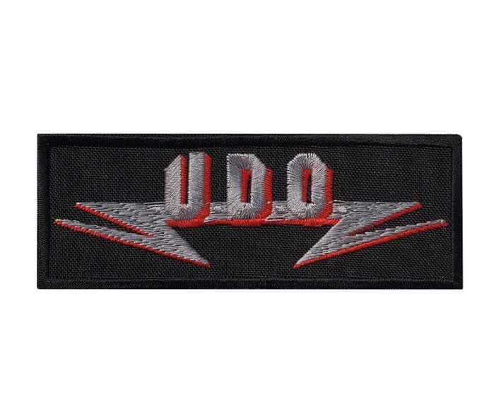 Правоъгълна нашивка U.D.O. със сребристо лого и червени сенки върху черна основа.