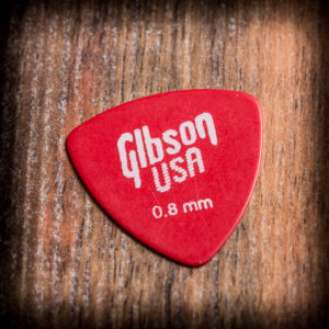 Червено перце за китара Gibson USA 0.8 mm с бяло лого върху дървена повърхност